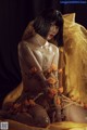 A woman sitting on a bed covered in gold and orange flowers.