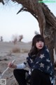 A woman sitting under a tree in the desert.